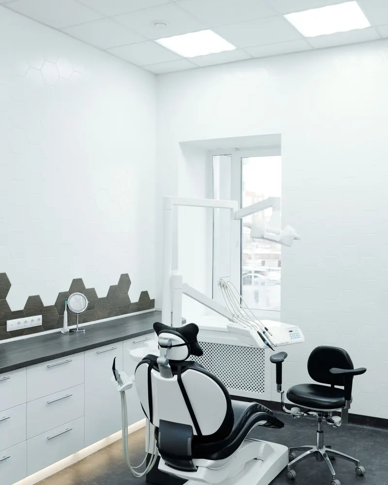 An empty dental treatment room with a white chair and a window.