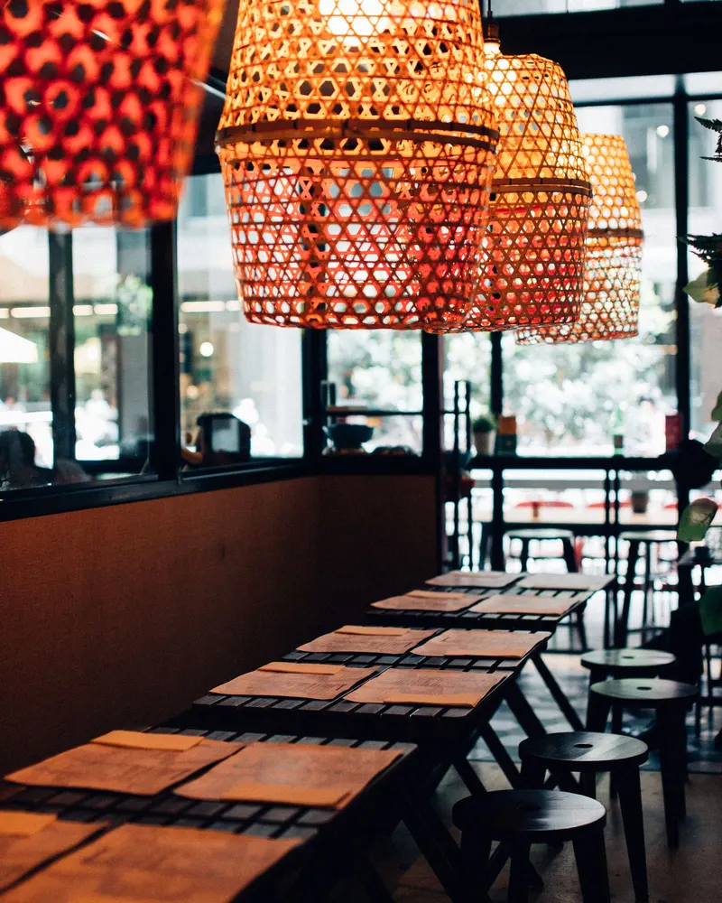 Empty restaurant tables under woven bamboo lampshades.
