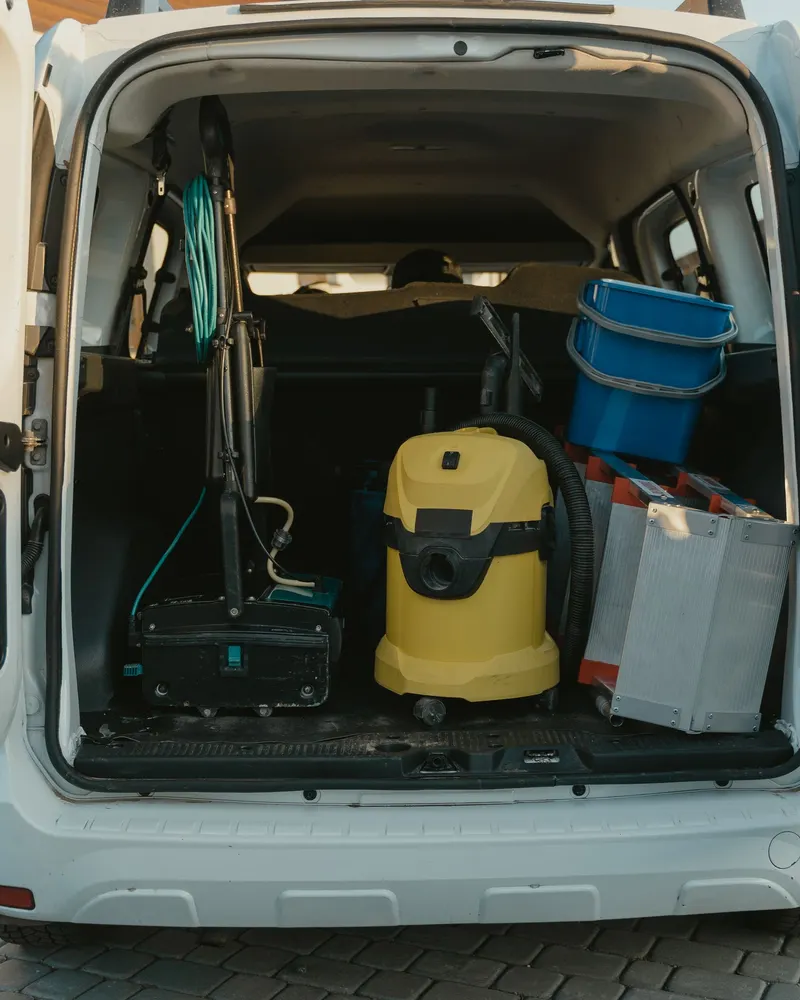 The open back of a white van loaded with cleaning and service equipment.